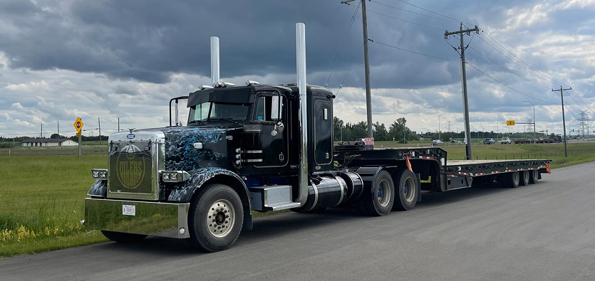 Custom black semi-truck with a lowboy flatbed trailer parked on an asphalt road, providing flatbed towing and specialized automobile transport by Action Towing Service.