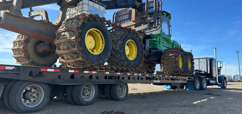 Close-up of heavy forestry machinery with chained tires loaded on a heavy haul transport trailer for heavy equipment shipping.
