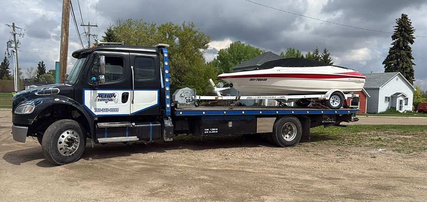Commercial flatbed tow truck providing premium boat transportation by hauling a powerboat on its trailer.